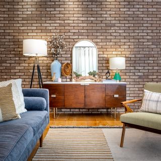 A living room with a brick wall, a mid-century style credenza, and a blue sofa