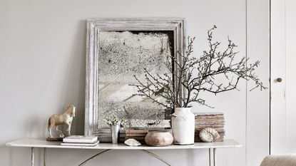White console table with foxed glass mirror, and white and wooden objects