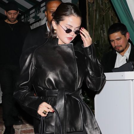 Selena gomez wears sunglasses and a belted leather jacket.