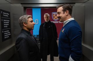 (L to R) Nick Mohammed as Nathan "Nate" Shelley and Jason Sudeikis as Ted Lasso stare at each other in an elevator while Anthony Head as Rupert Mannion looks on from outside the elevator in the first photo released from Ted Lasso season 3.