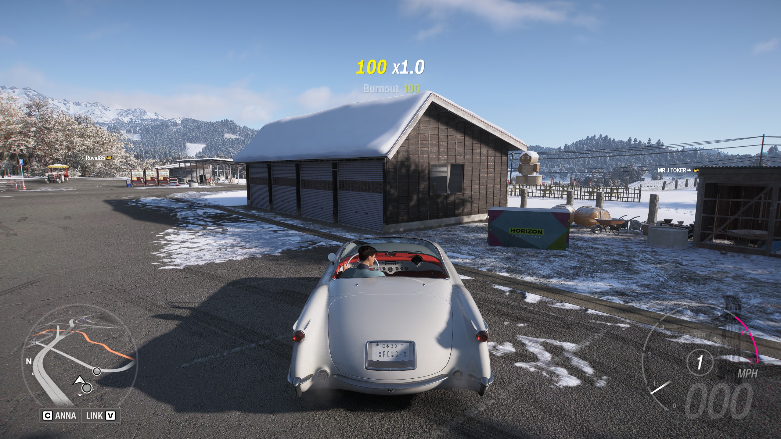  A white classic car parked next to a treasure chest outside a wooden building in a snowy field.