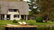 a thatched cottage on the edge of a pond in Normandy, France surrounded by greenery, tree, ducks with a deck for sunbathing
