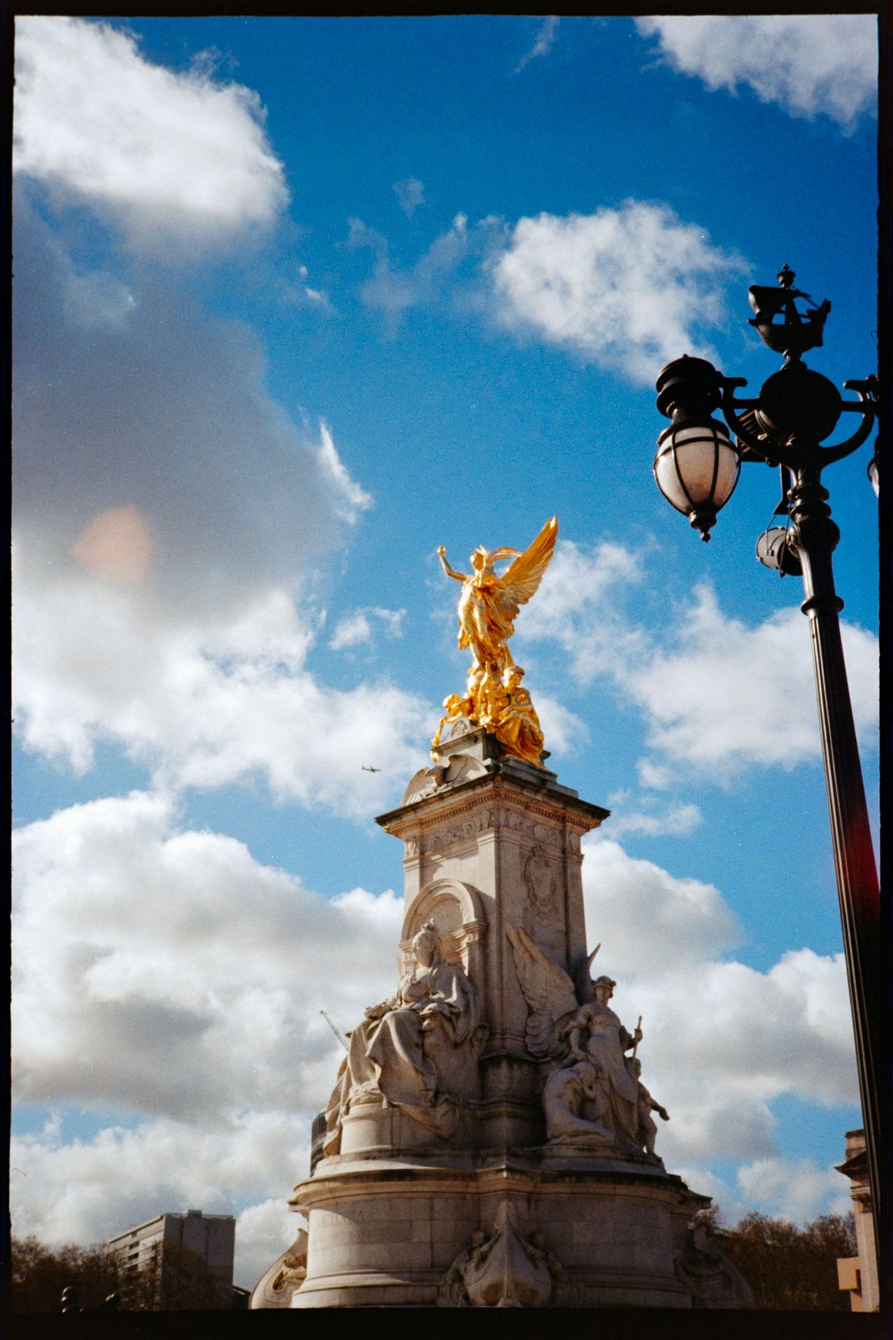 The Victoria Memorial outside Buckingham Palace, with its gold statue lit by sunlight against a blue sky.