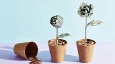 Coins spill out of a flower pot next to two other pots containing coins and origami dollar flowers 