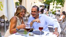 A happy retired couple is dining out, drinking wine at a nice restaurant. They are smiling and looking at her smartphone.