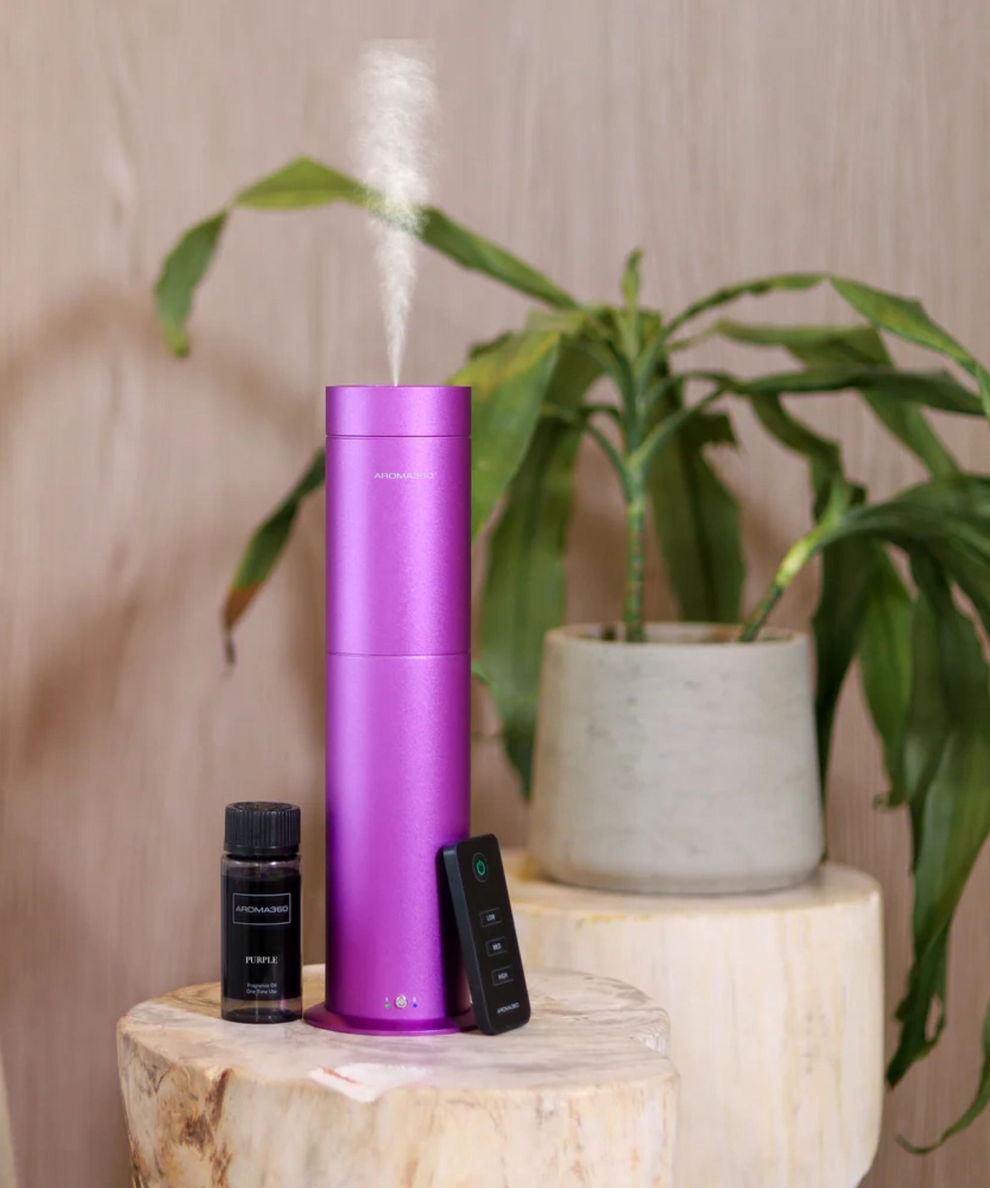 Pink Aroma360 Wireless Pro Scent Diffuser on a wooden stool with houseplant behind.