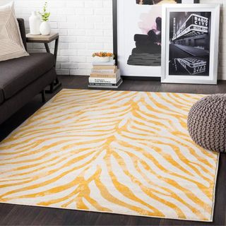 A white and yellow zebra-print rug sits on top of a dark gray floor, next to a gray couch