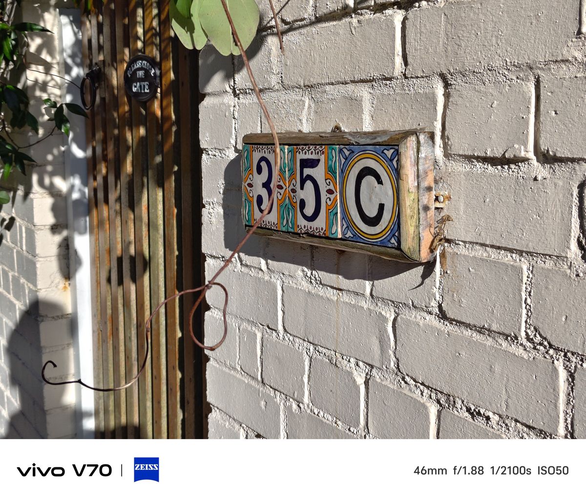 Decorative ceramic house number sign reading &ldquo;35C&rdquo; mounted on a white brick wall in sunlight.
