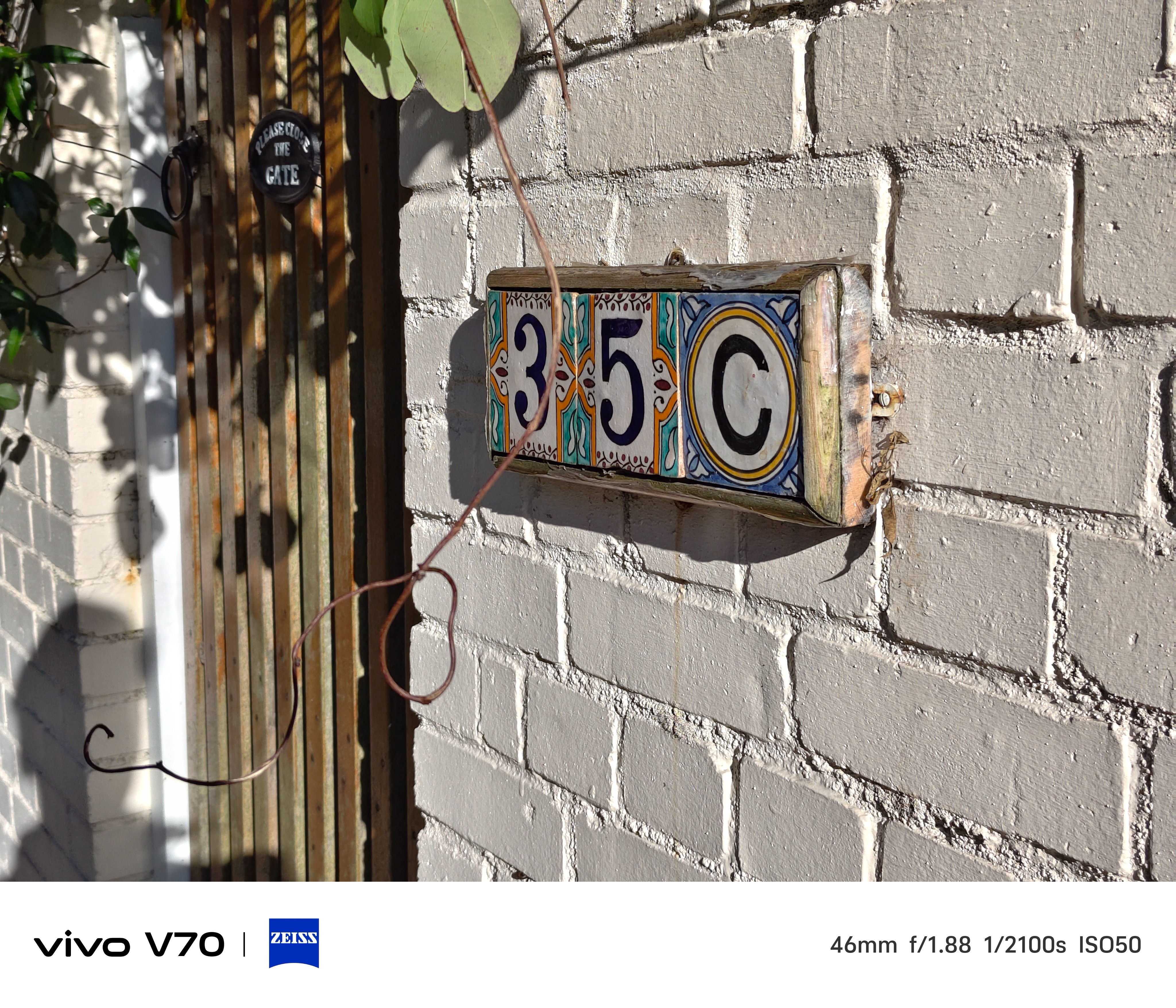 Decorative ceramic house number sign reading “35C” mounted on a white brick wall in sunlight.