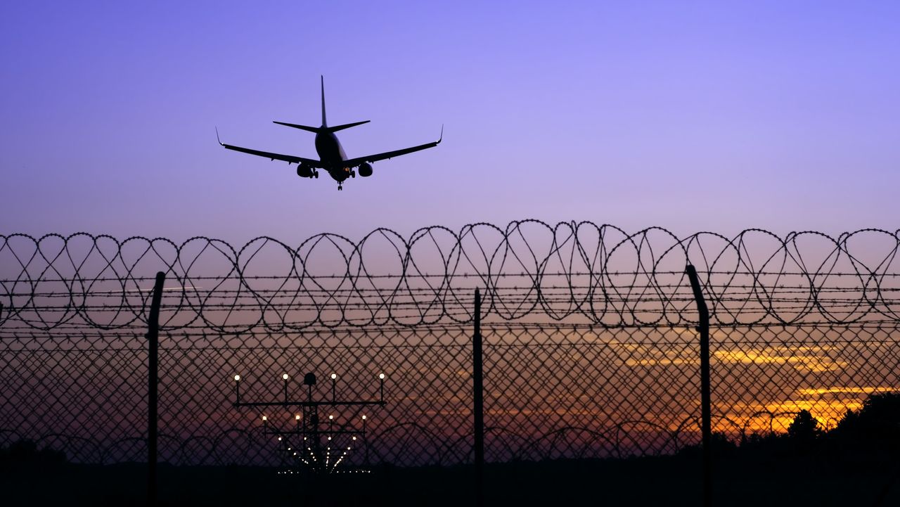 Jet airplane in the distance landing at sunset behind fence