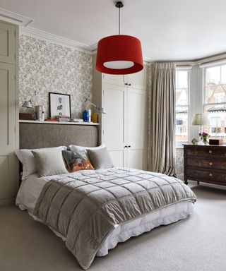 A neutral bedroom with a large double bed with a throw and cushions below a red ceiling light