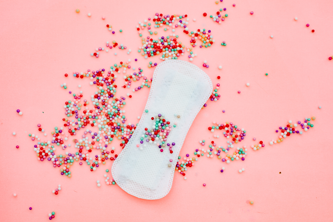 A sanitary pad on a pink background with sweets