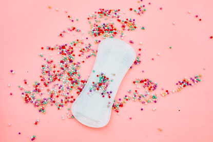 A sanitary pad on a pink background with sweets