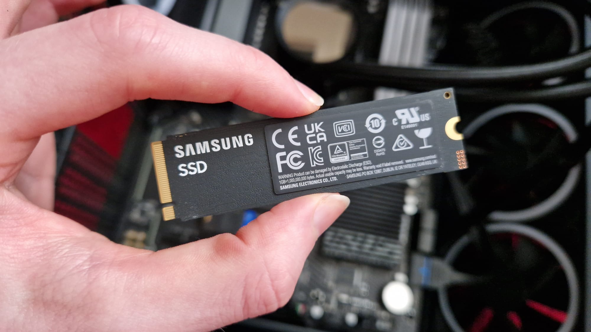 A Samsung 9100 Pro review image showing the SSD being held above a motherboard