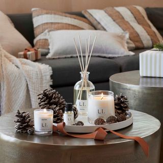 scented candles and diffuser on a tray surrounded by pine cones