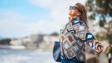 An older woman stands outside and opens her arms to the wind.