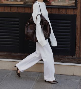 Annemiek Kessels wearing a white sweater and white jeans with a pair of black heels and a brown bag.