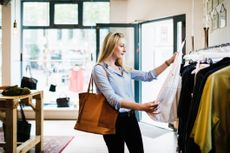 A woman looking at a white blouse on display in a clothing store while out shopping for the day.