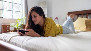 A woman wearing a yellow top plays Tetris on her phone in bed
