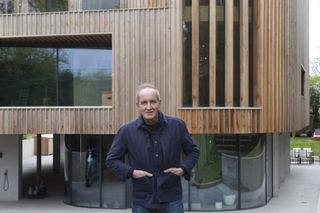 Kevin McCloud from Grand Designs standing outside a new wooden building