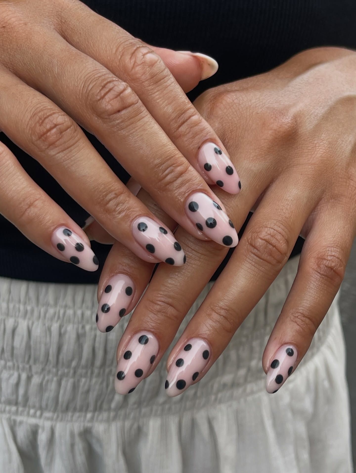 Sheer pink almond nails covered in big black polka dots