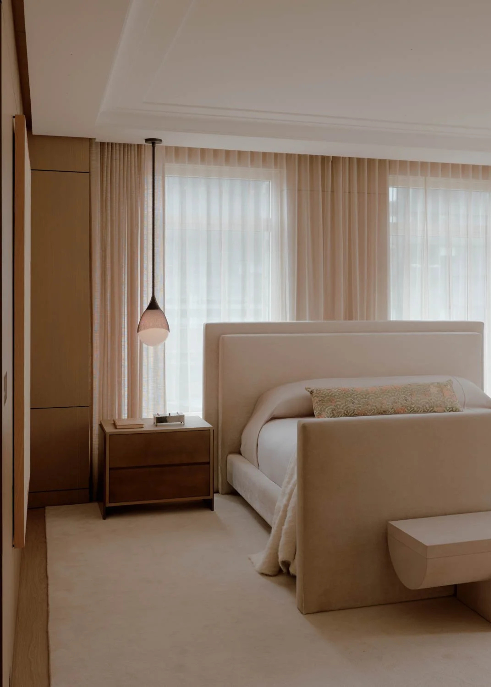 A minimalist bedroom with sheer window treatments, a hanging pendant lamp over a wood bedside table