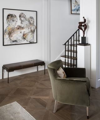 A modern hallway idea with leather entryway bench, green velvet armchair and sculpture on plinth