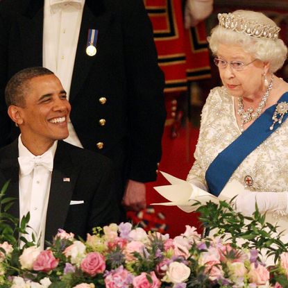 Queen Elizabeth wearing a tiara giving a speech standing up at a banquet table next to Barack Obama