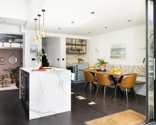 A kitchen extension with a small marble effect island below pendant lighting and a dining area with tan leather chairs