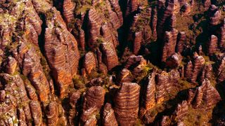 Aerial view of the Bungle Bungles in Western Australia. We see towers of orange and gray striped stone with vegetation growing in between.