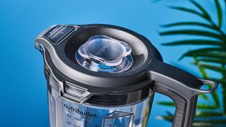 a black nutribullet with a big blending component is photographed in front of a blue backdrop, showing its plastic pitcher jug, silver blades, and tamper