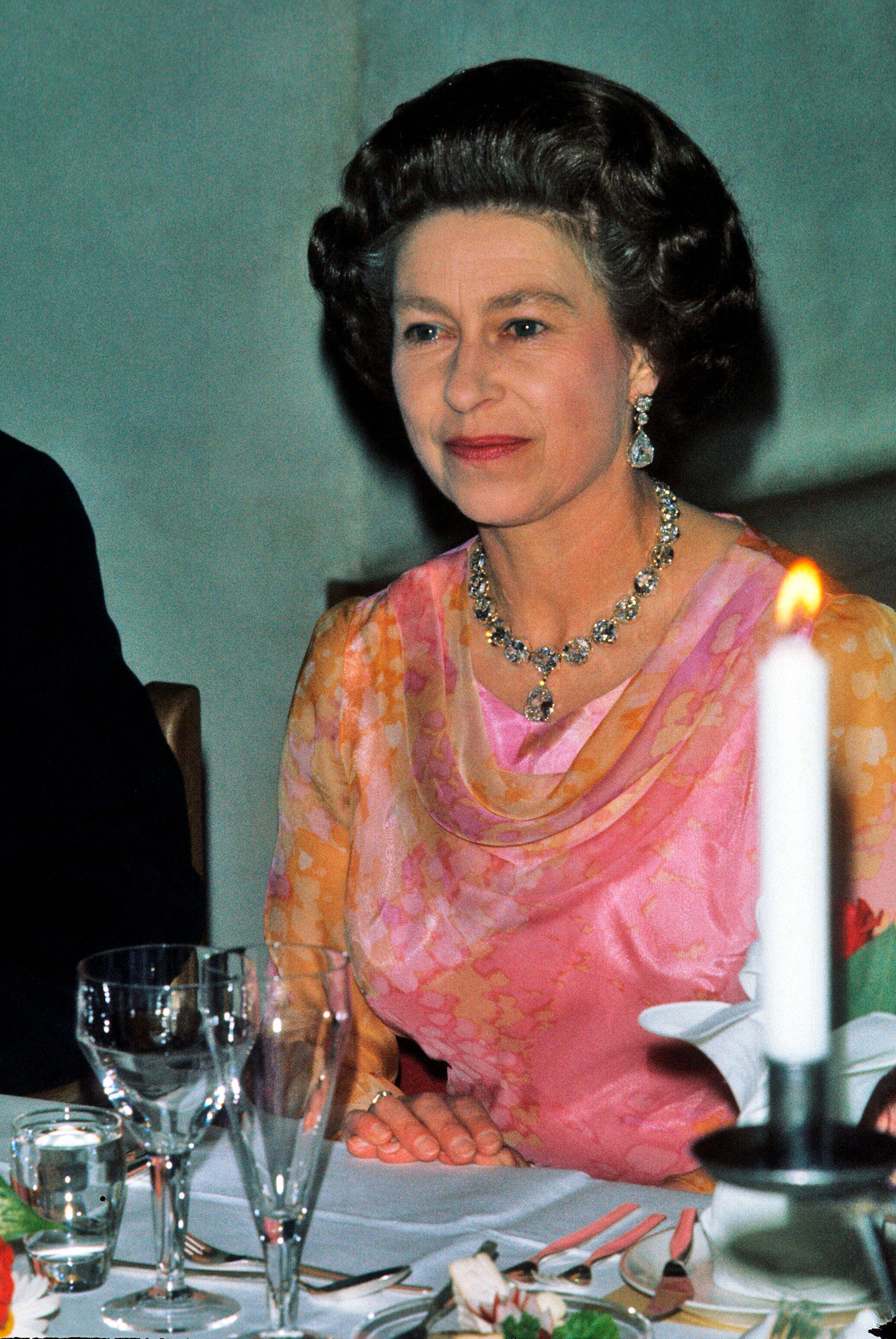 Queen Elizabeth sitting at a candle lit banquet table in a pink and orange gown