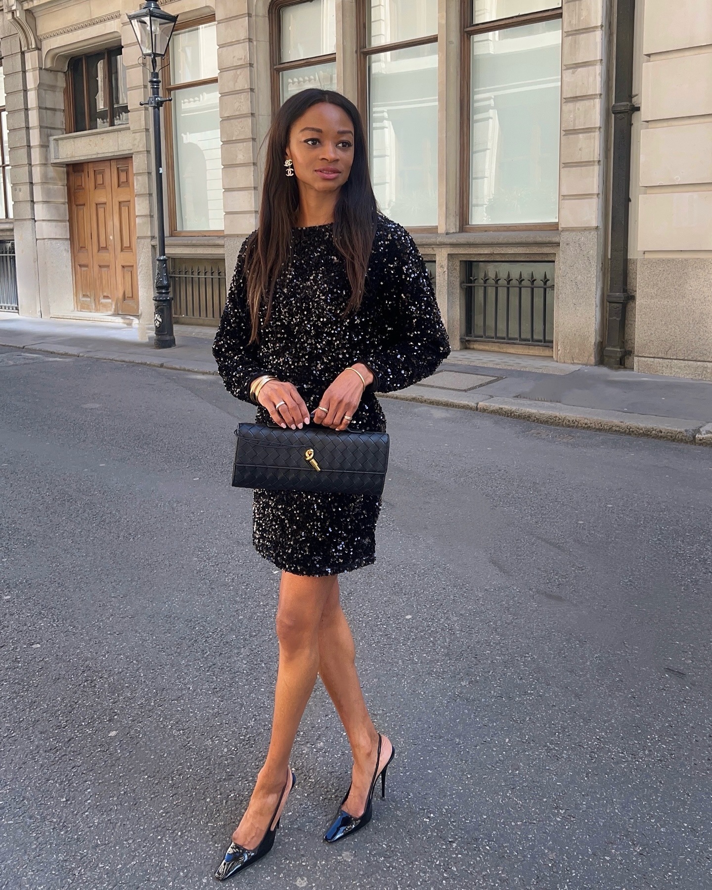 Woman wears sparkly dress, black heels and carries bottega andiamo clutch