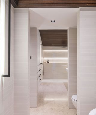 A narrow white bathroom with LED ceiling and wall lights