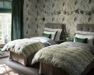 Gray twin beds in front of white, gray and green floral wallpaper