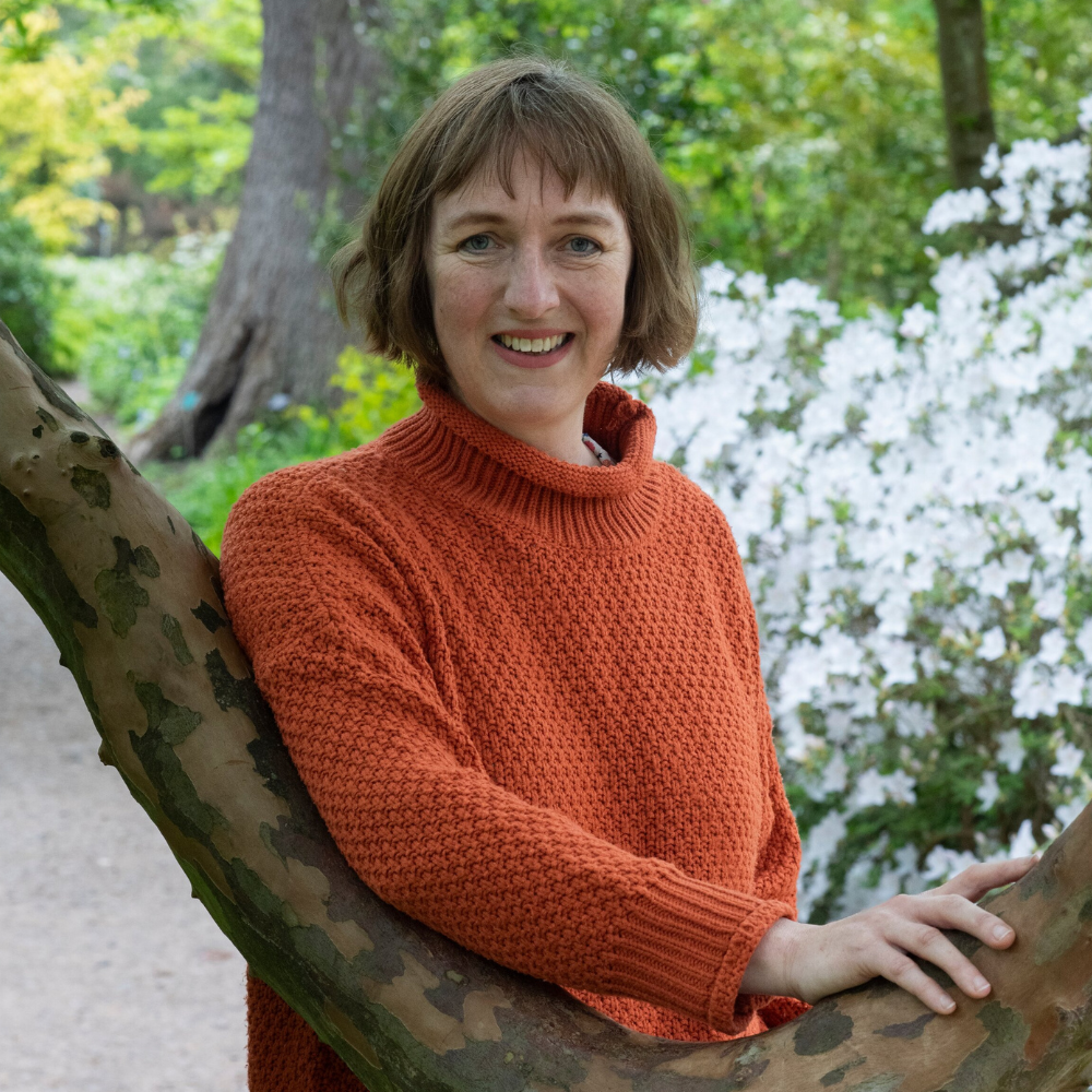 Helen Bostock with her hand on a tree and flowers in the background
