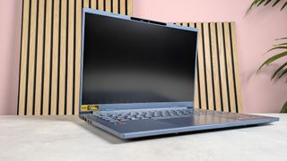 Three-quarter view of Acer Aspire 14 AI (2025) open on desk with wooden panel, plant, and pink wall in background