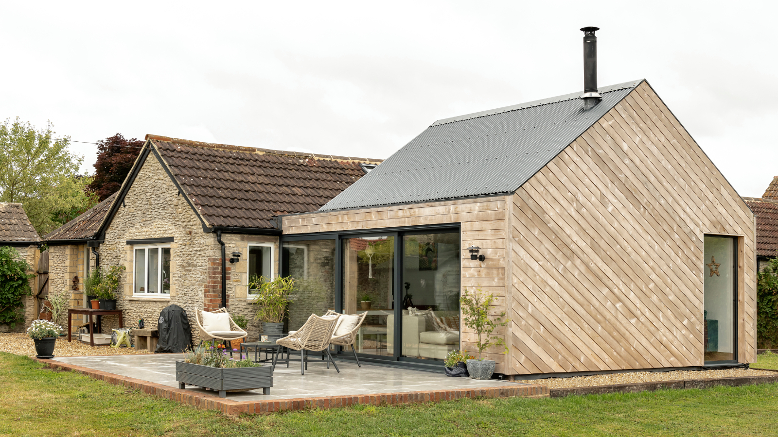 extension to stone cottage clad in diagonal timber strips on side, with timber shingles to front elevation, corner glazing