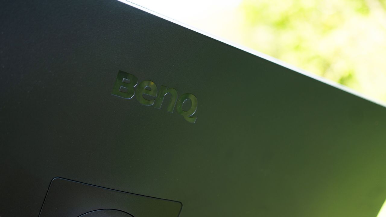 A black BenQ PD3225U monitor sitting on grass in sunshine