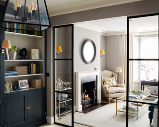 Cream fireplace in living room with crittal-style black framed doors, mirror and drinks trolley