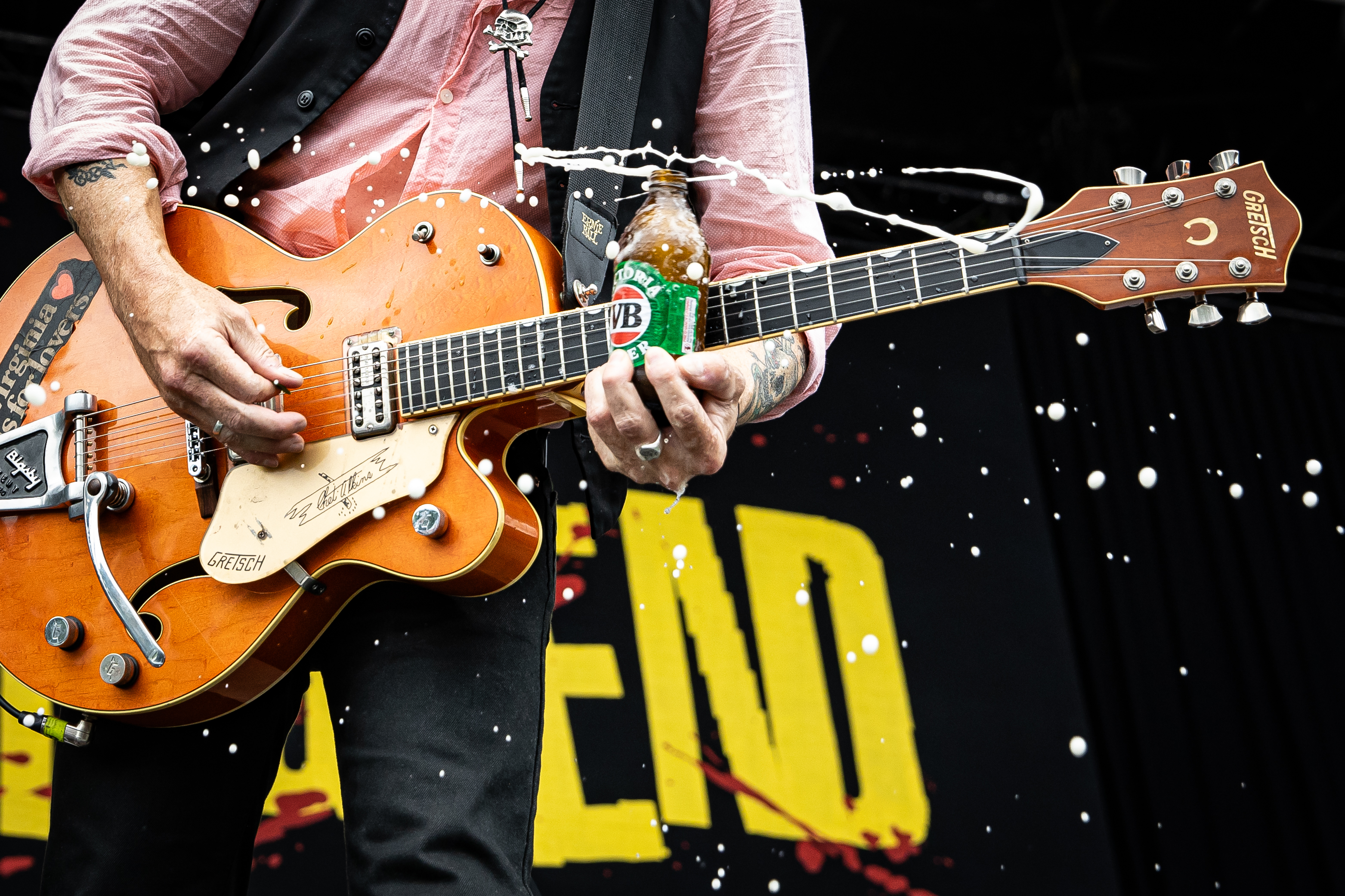 A man playing a Gretsch electric guitar with a bottle of VIctoria Bitter beer