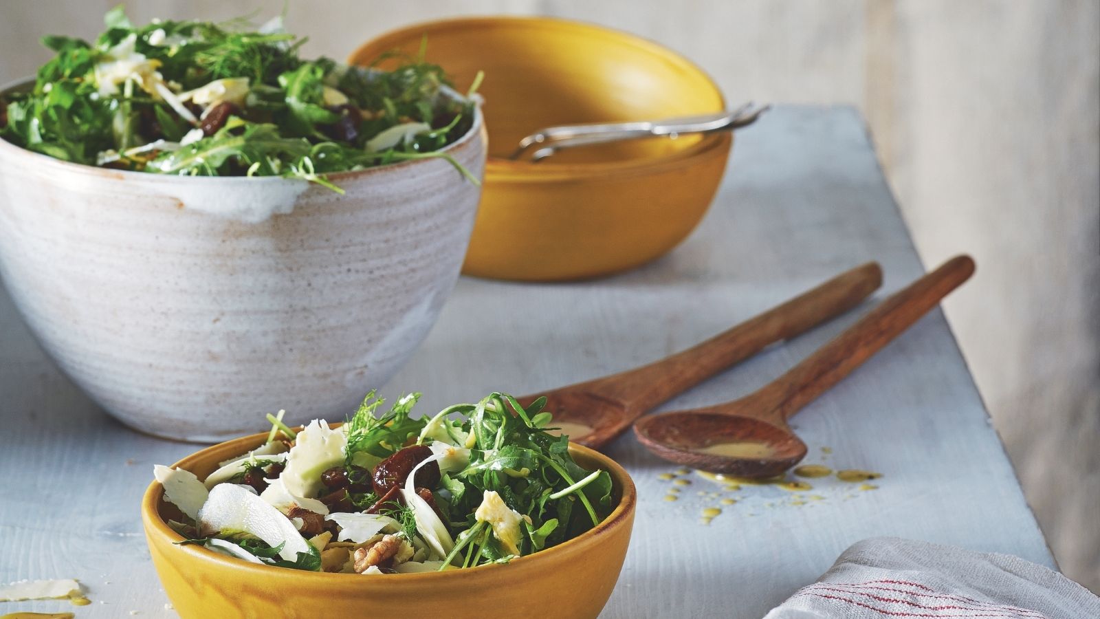 Table with white ceramic serving bowls and yellow ceramic bowls of salad