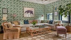 a green floral wallpapered family room with a large sectional couch, diamond woven rattan rug, wicker furniture and eclectic artwork