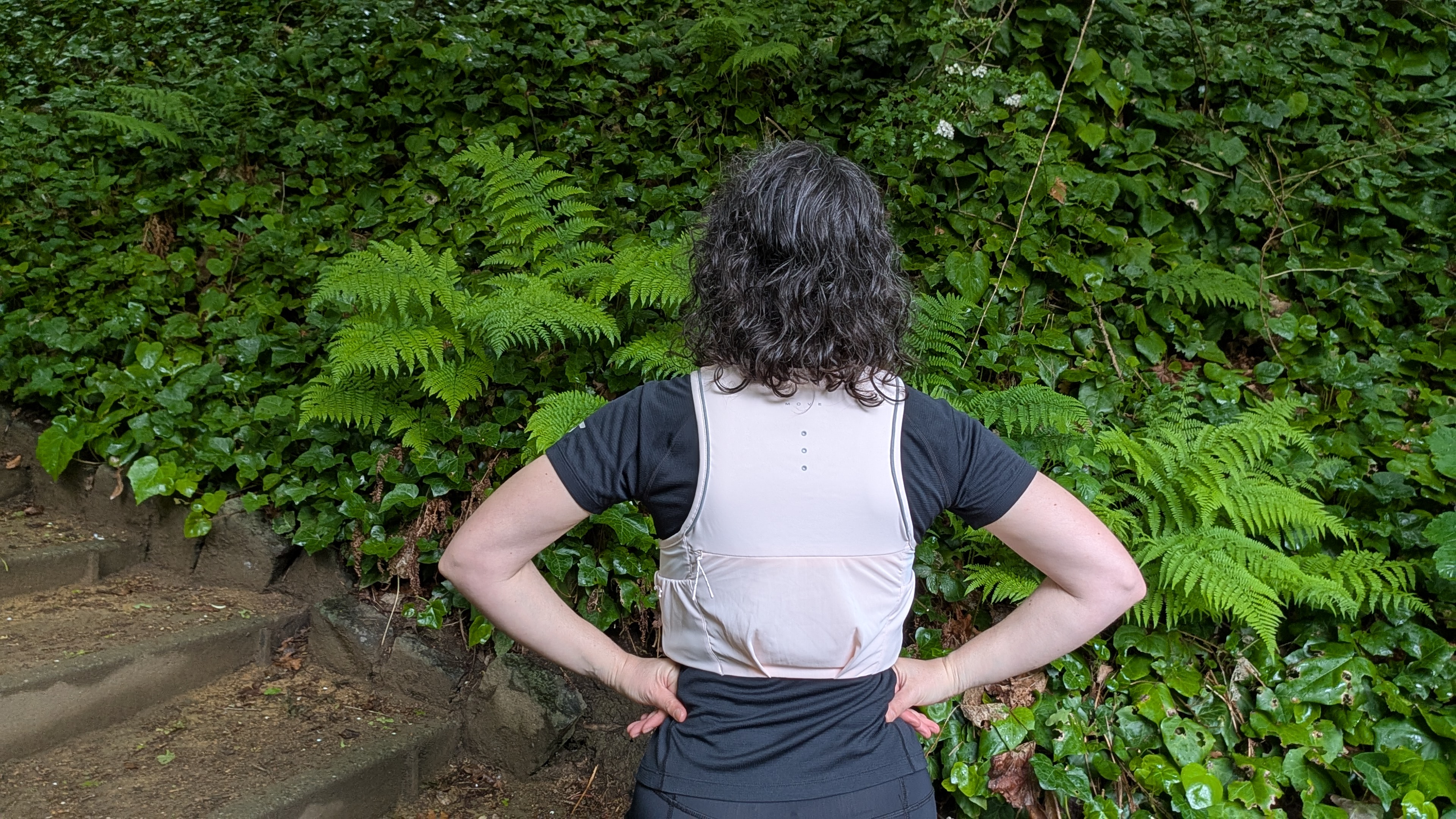 Shown from behind, a woman dressed for running in black clothing with a pink H&M Move Lightweight Running vest