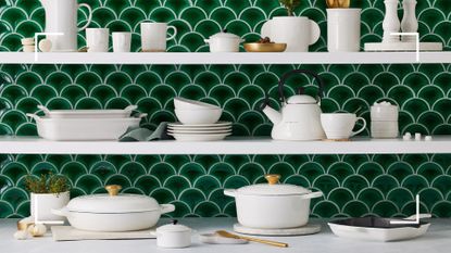 Le Creuset white cookware collection on shelves in an emerald green tiled kitchen