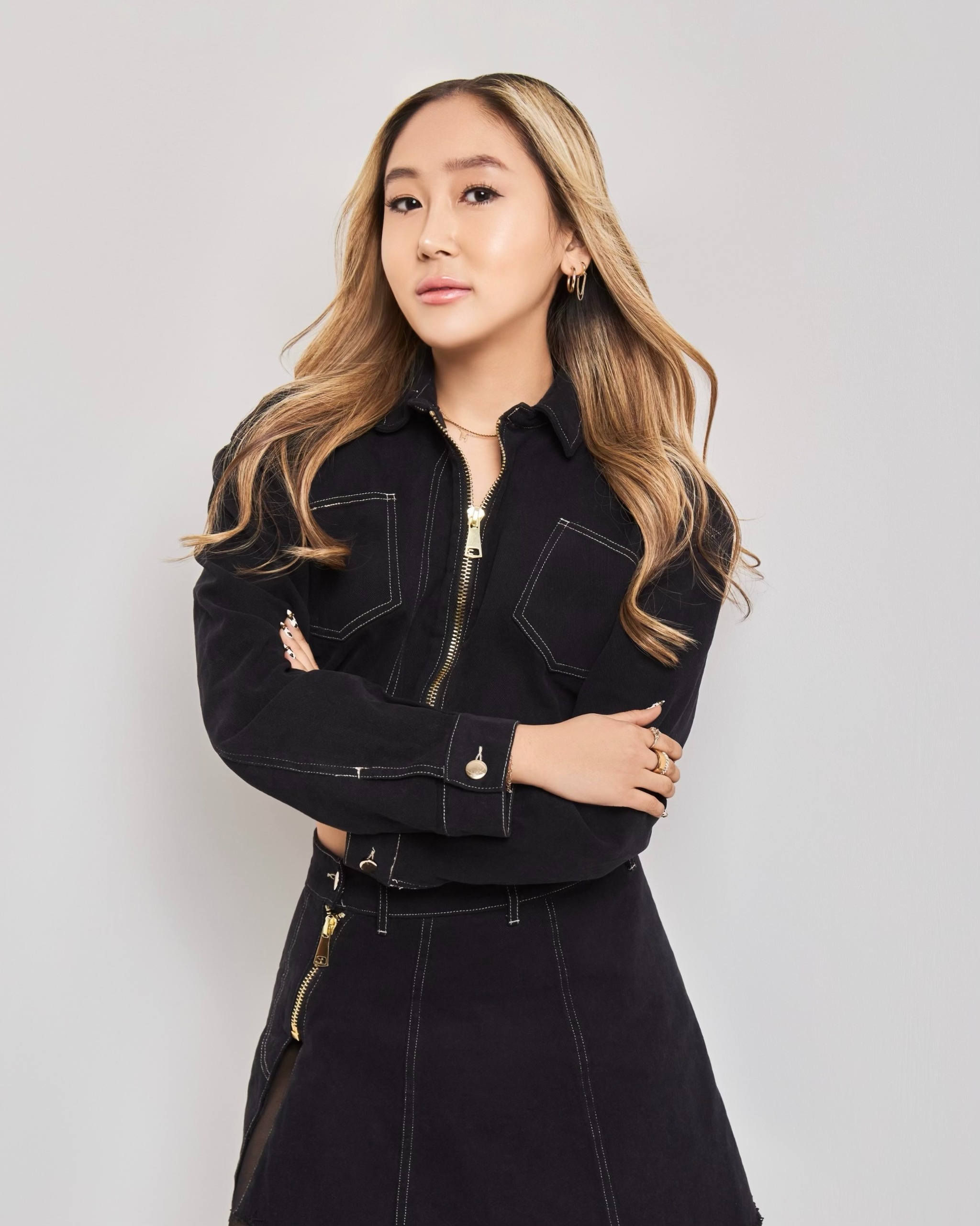 an asian woman with blonde hair in a dark denim jacket and skirt