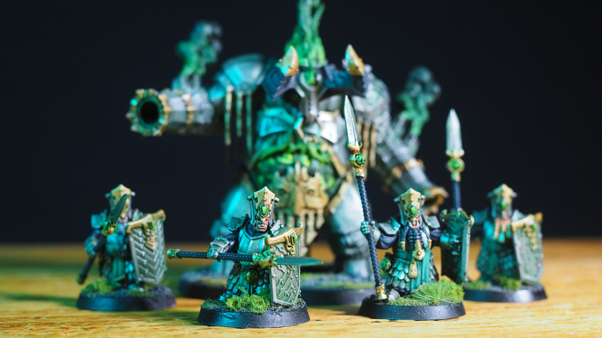 Helsmiths of Hashut warrior models on a wooden surface, with a bull-like construct behind them