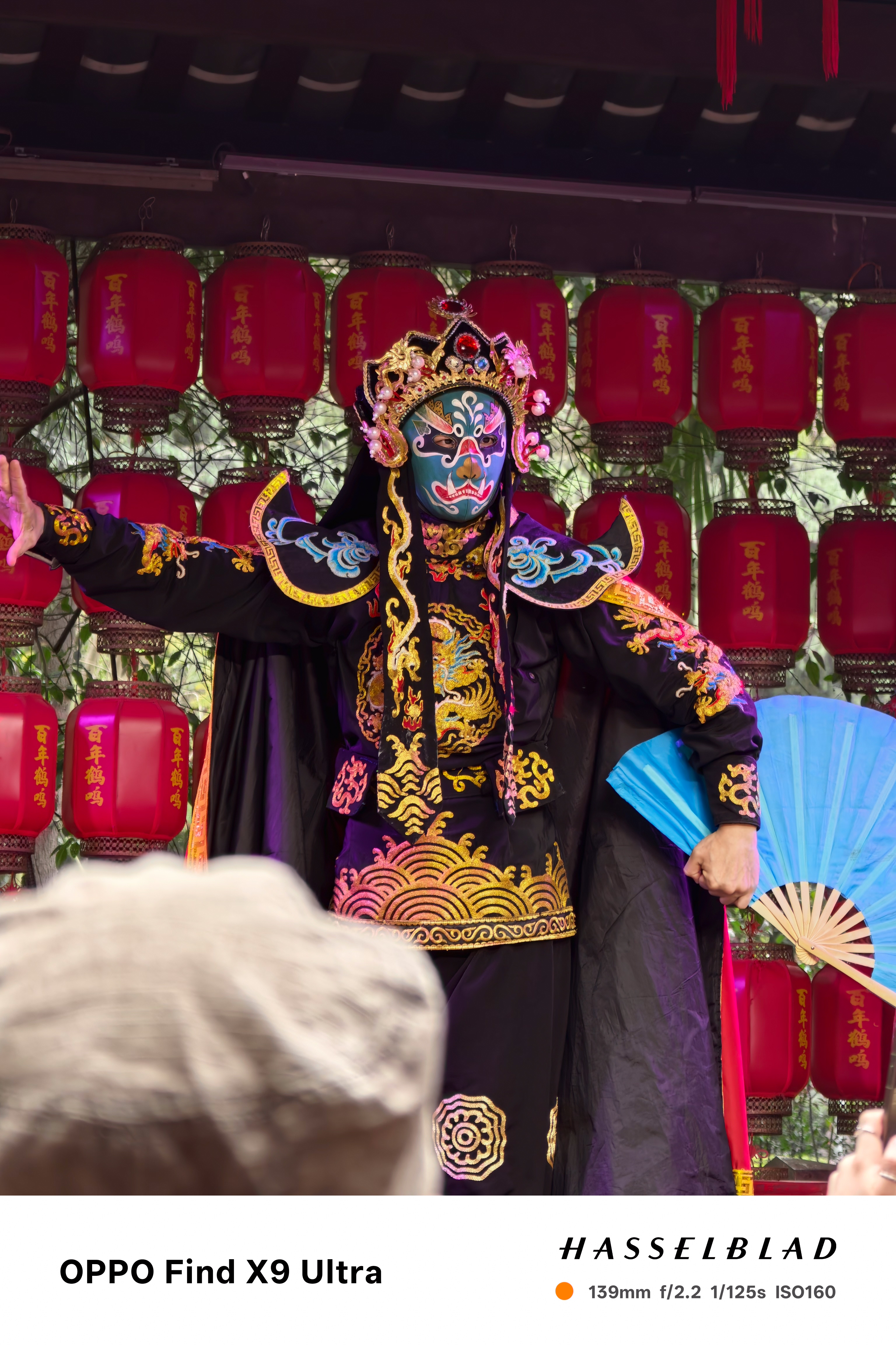 Sichuan opera performer in ornate costume posing onstage before red lanterns