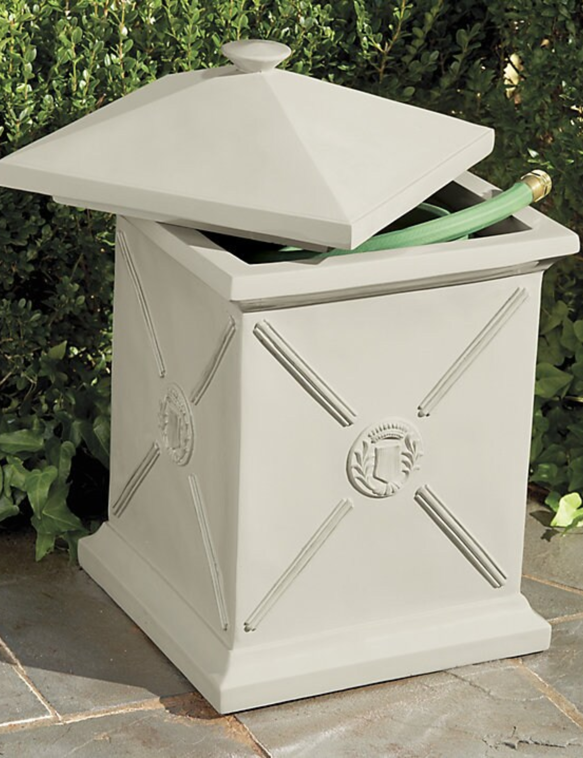 Antique-style hose pot styled atop a stone patio area with hedge