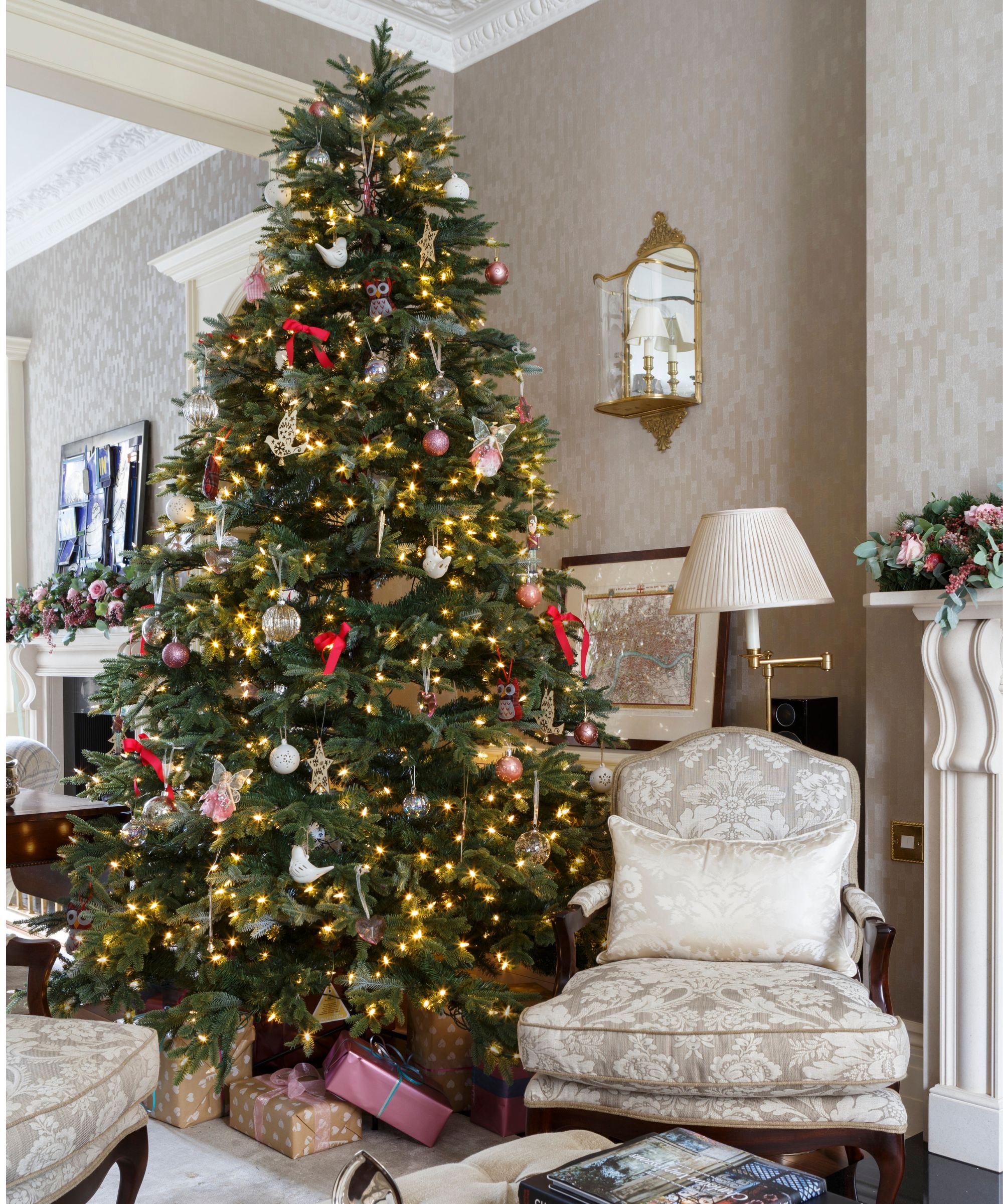 Christmas tree with yellow lights and red and white ornaments, in a living room with cream and white floral armchairs